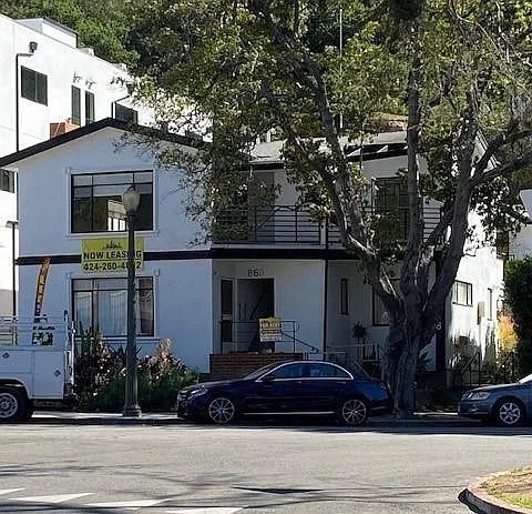 A two-story white house with a black car parked in front.